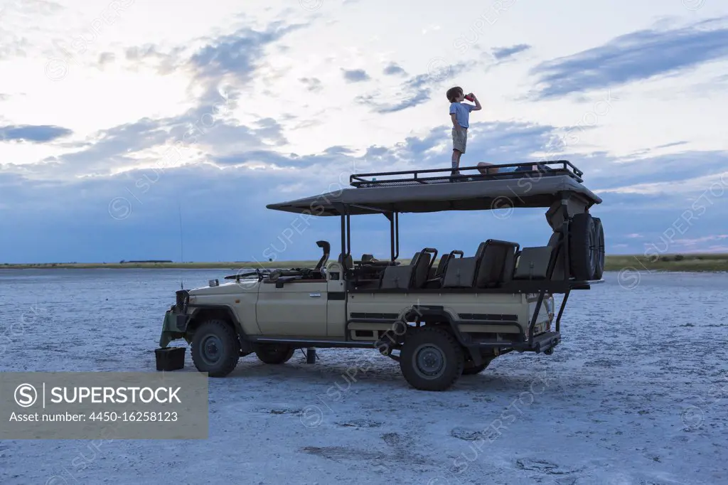 Six year old boy and older sister standing on top of safari vehicle, Nxai Pan, Botswana