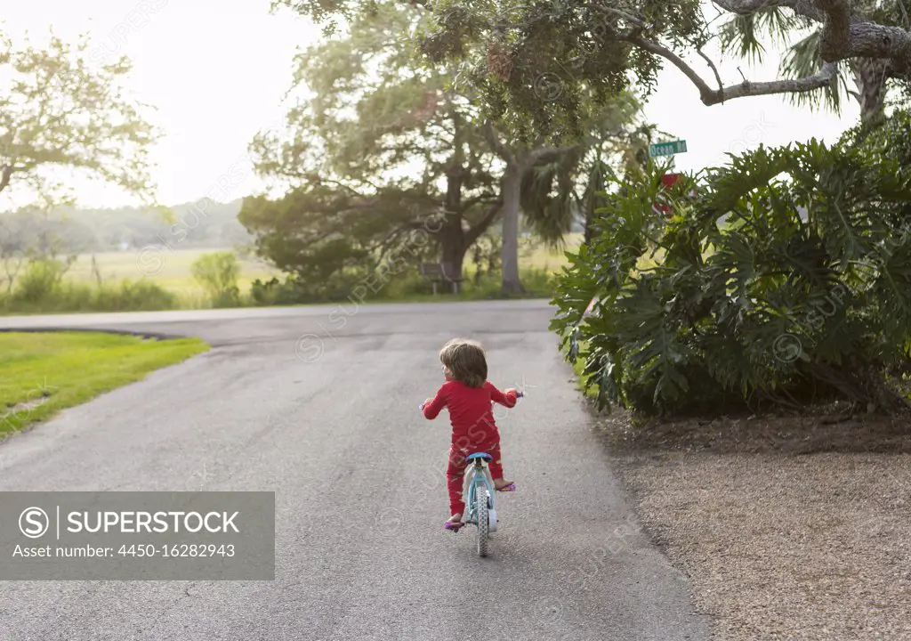 A five year old boy in a red shirt riding his bike on a quiet residential street. 