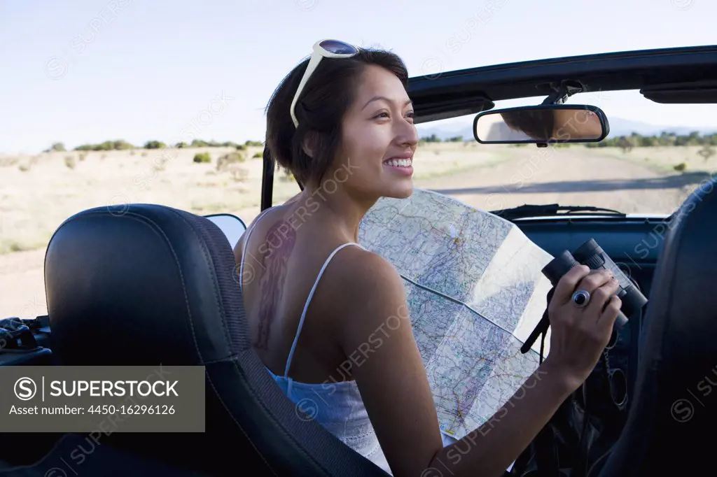 Native American woman in sun dress looking at a map in the passenger seat of a convertible.