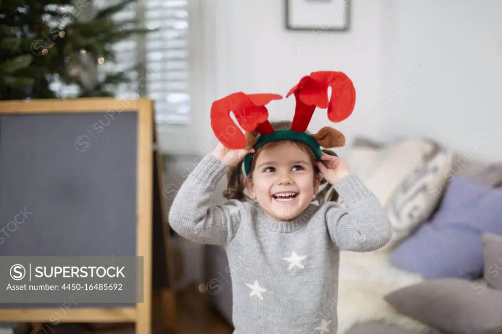 Smiling young girl wearing grey jumper putting on reindeer antler headband.