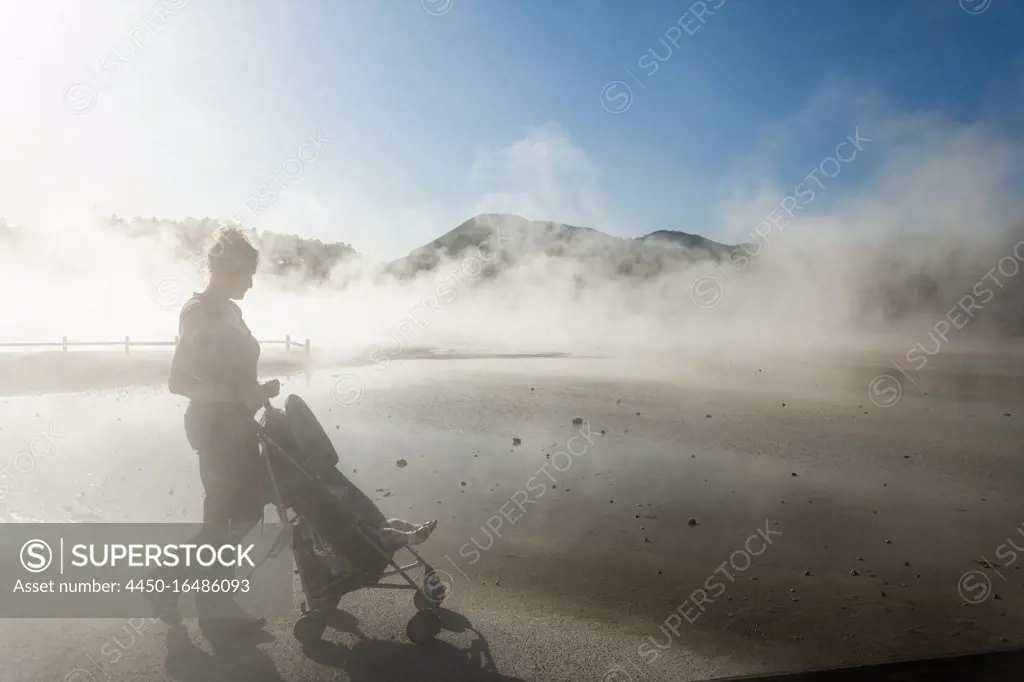 A woman and a child in a buggy in rising steam from thermal pools