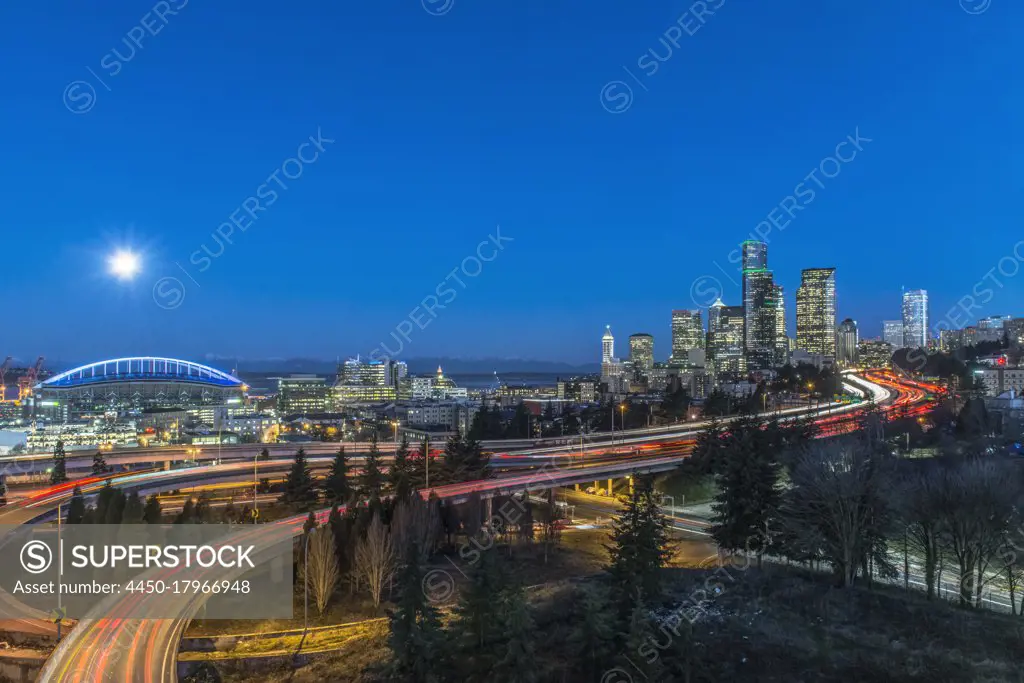 The city skyline of Seattle at night, road and bridge, downtown buildings lit up in moonlight.