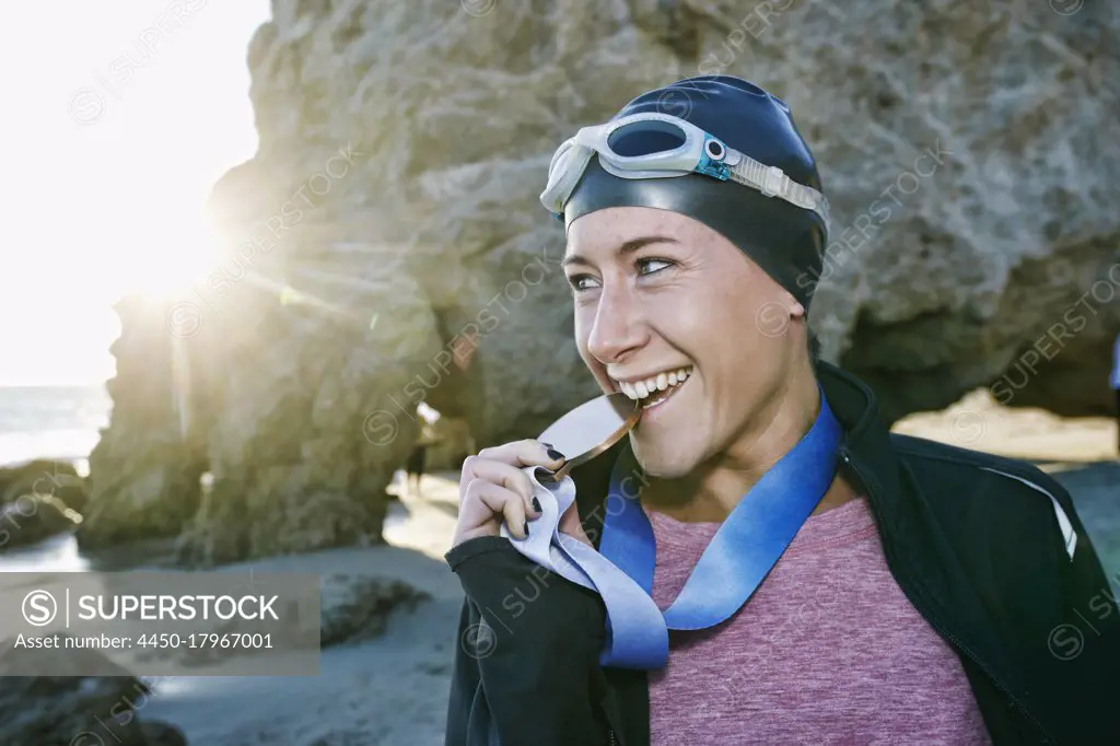 Young woman, triathlete in jacket biting a large medal with her teeth, a winner