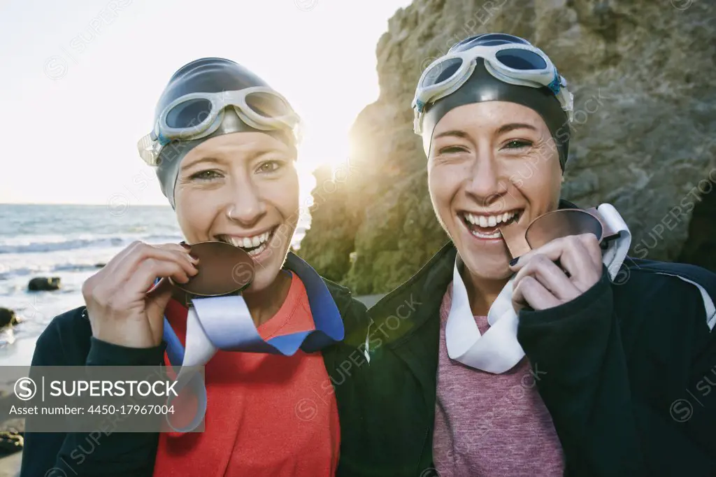 Two sisters, triathletes in swimhats and goggles wearing their large medals, winners. 