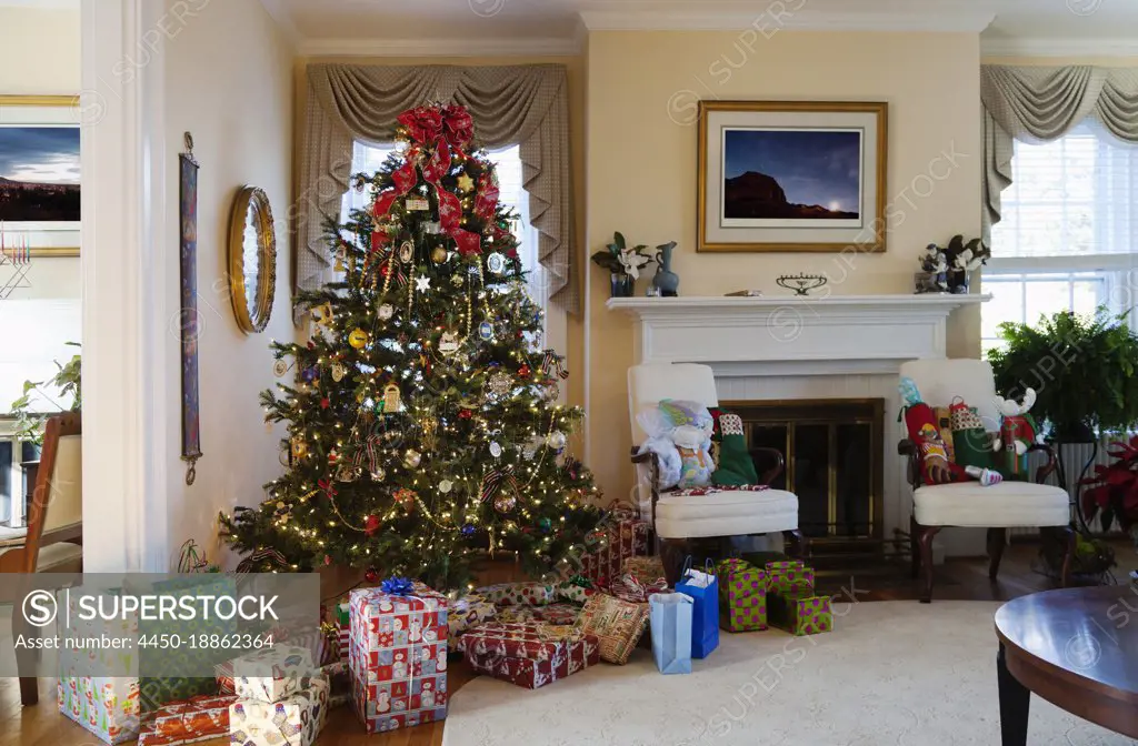 Living room with Christmas tree and gifts, traditional decorations, fireplace and furniture.