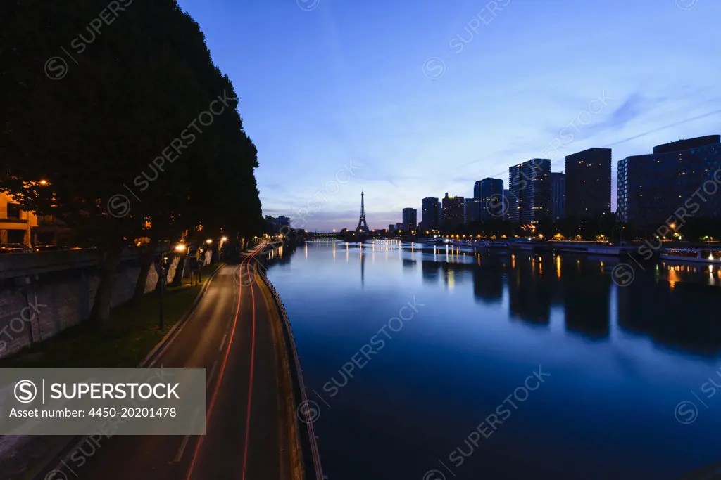 View along the River Seine to the Eiffel tower, the river embankment, and the city at dusk, reflections on the water. 