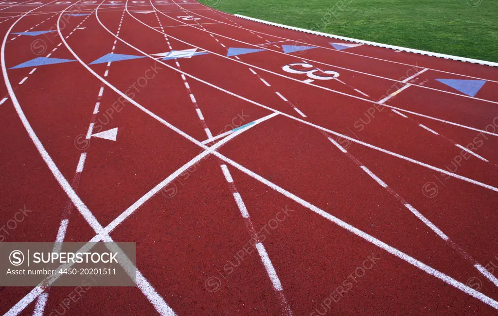 A red artificial surface running track. A sports ground. Painted marked lines for lanes.