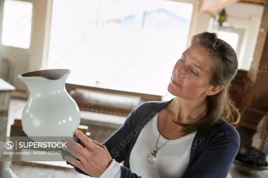 A woman holding a white pottery jug in an antique goods and furniture store.  High Falls, New York, USA