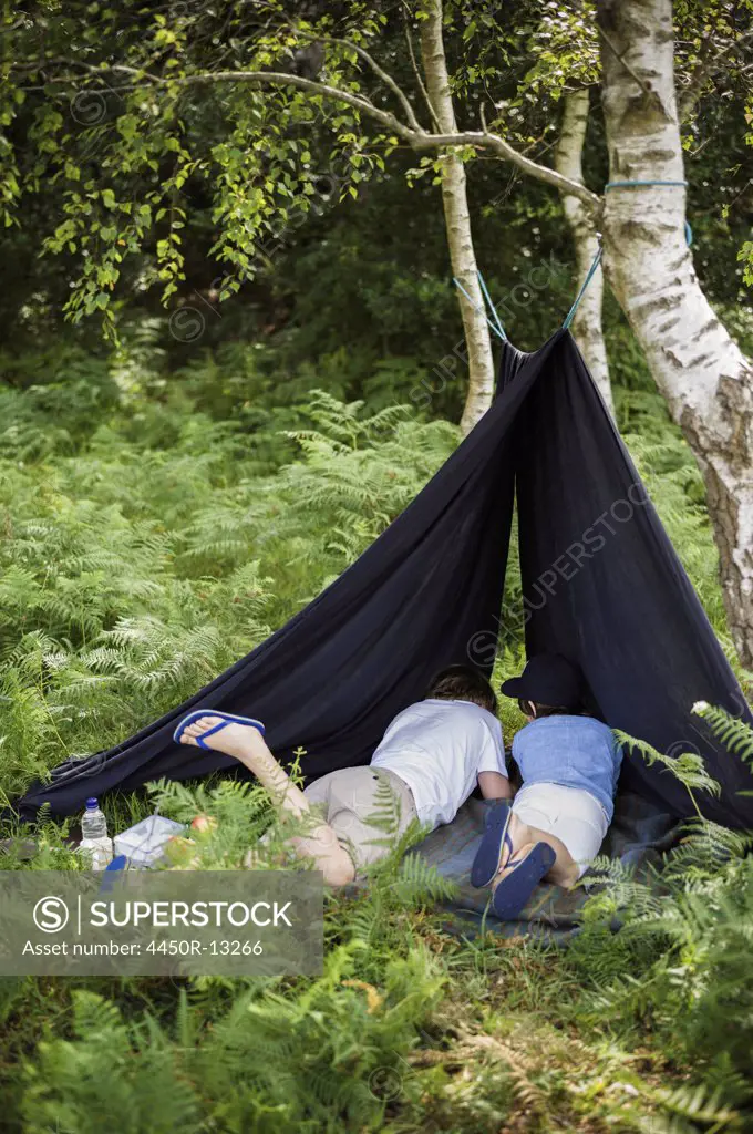 Two boys camping in the New Forest lying under a canvas shelter. Hampshire, England. 08/06/2013