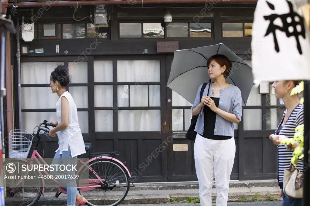 Woman standing outdoors, holding an umbrella.