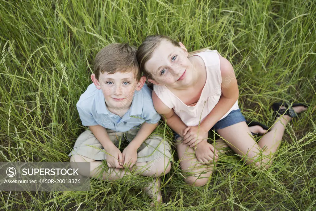 Brother and sister sitting side by side, in long grass.