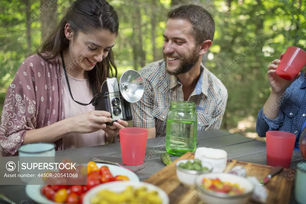 A group of people seated at a meal around a table outdoors. A couple side by side, one holding a camera with separate metal flash unit.