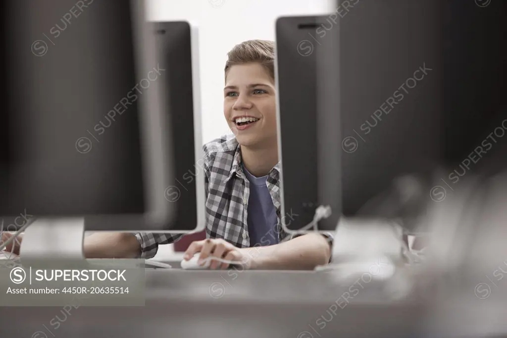 A school room, computer laboratory or lab with rows of computer monitors and seating. A young person seated working at a terminal.