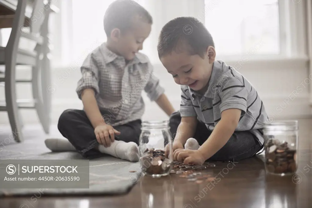 Two children playing with coins, dropping them into glass jars.