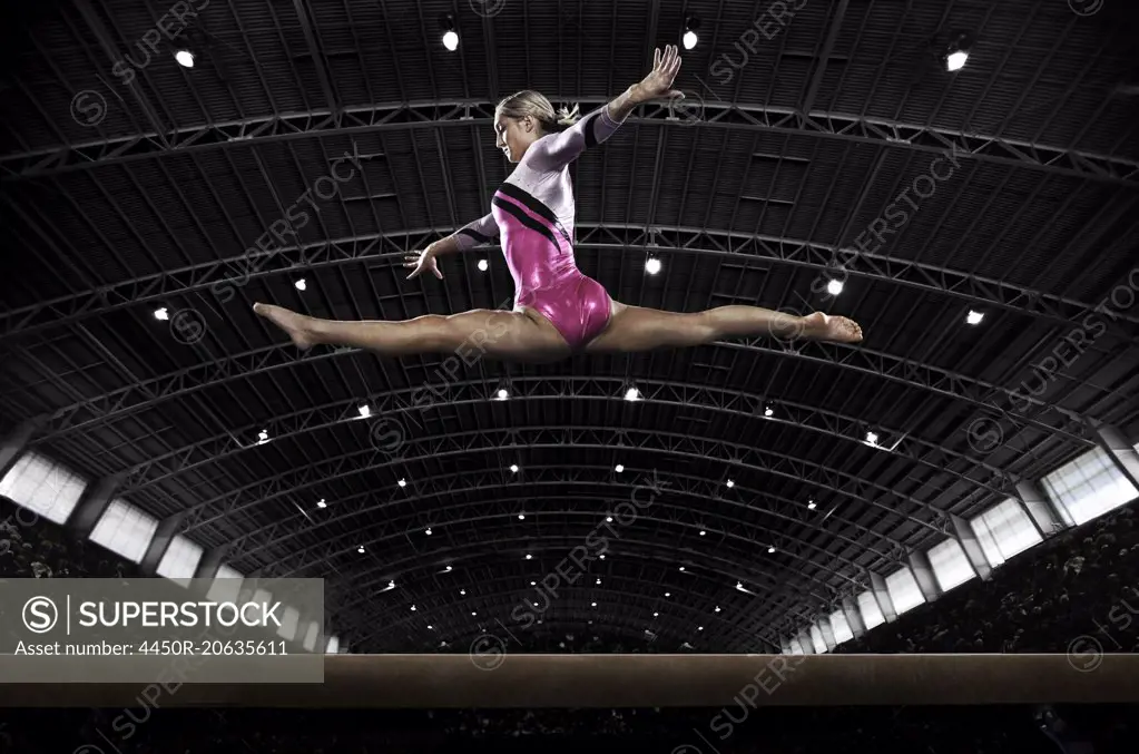 A young woman gymnast performing on the beam, balancing on a narrow piece of apparatus.