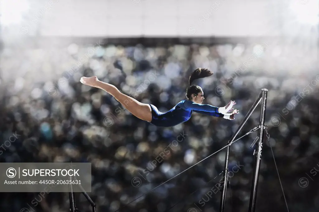 A female gymnast, a young woman performing on the parallel bars, in mid flight reaching towards the top bar.