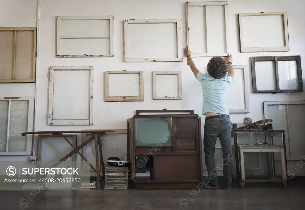 Loft decor. A man hanging framed picture canvases on a wall.