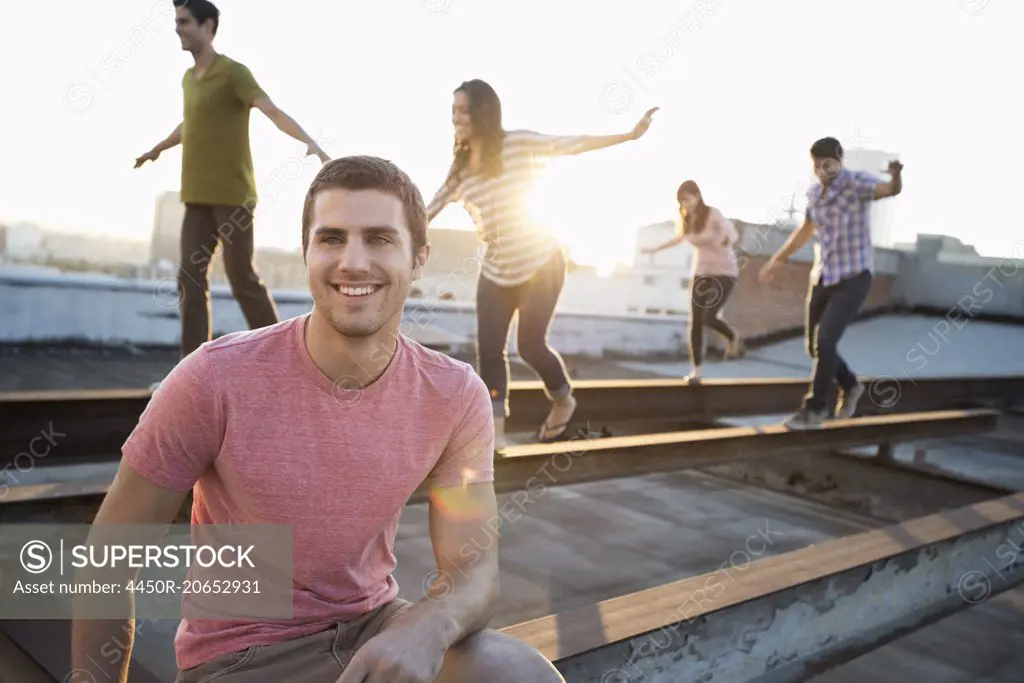 A group of people on a rooftop in the city at dusk, balancing and walking along steel struts on the roof.