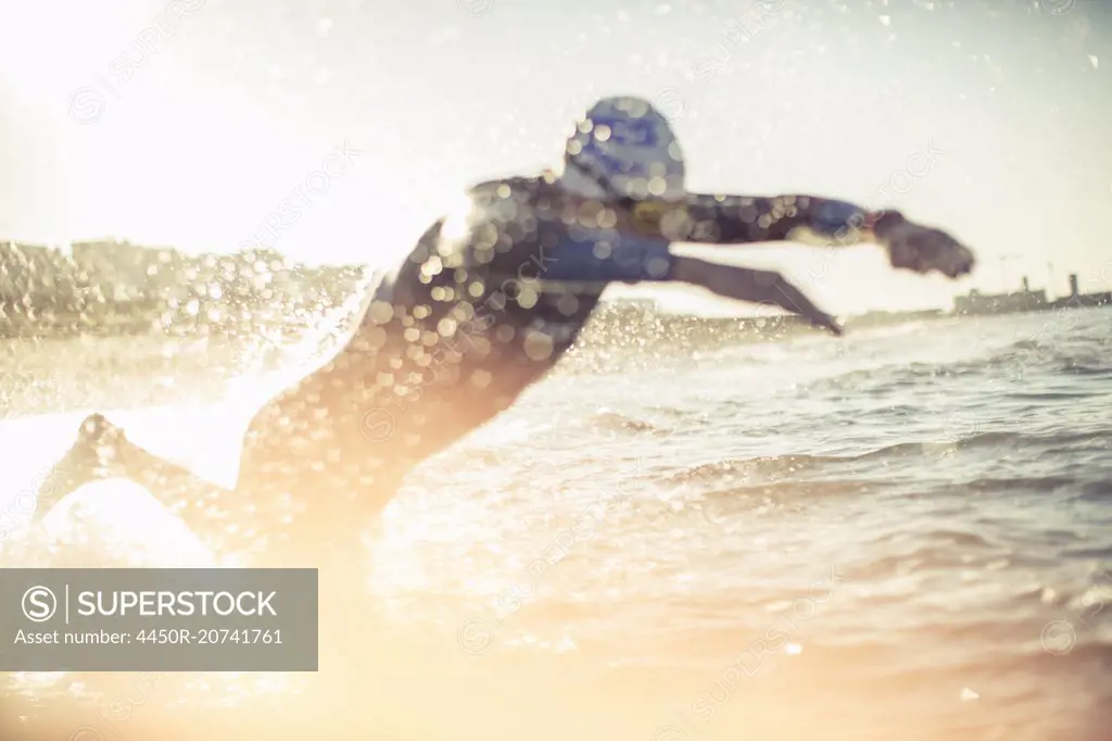 A swimmer in a wet suit running into the water, making a splash.