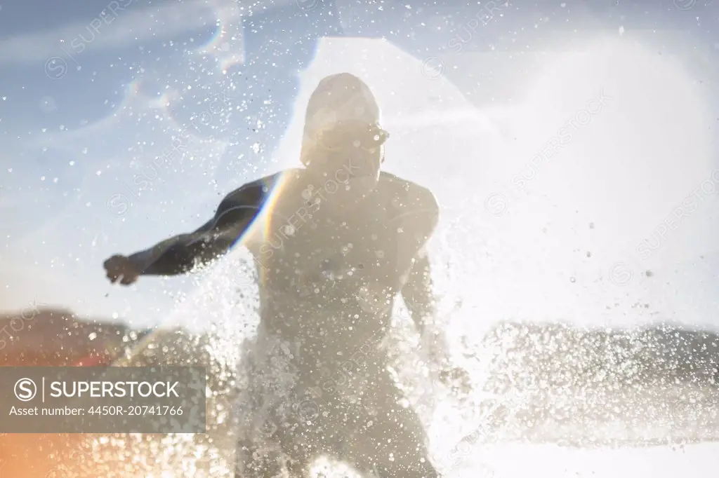 A swimmer in a wet suit running into the water, making a splash.