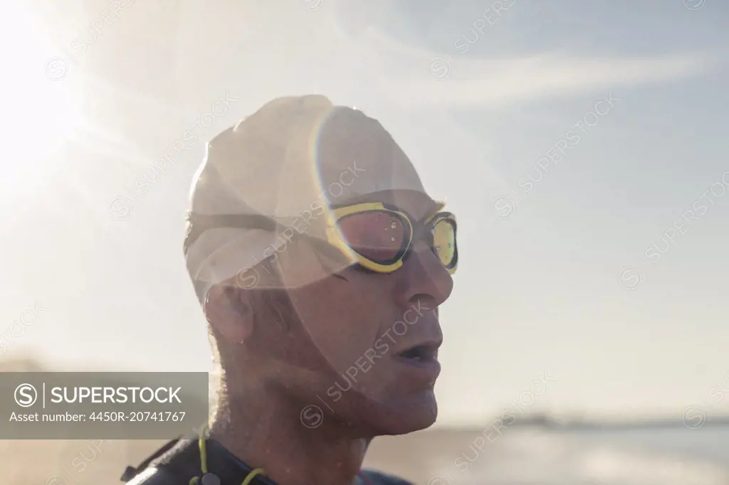 A swimmer in a wet suit, swimming hat and goggles on a beach.