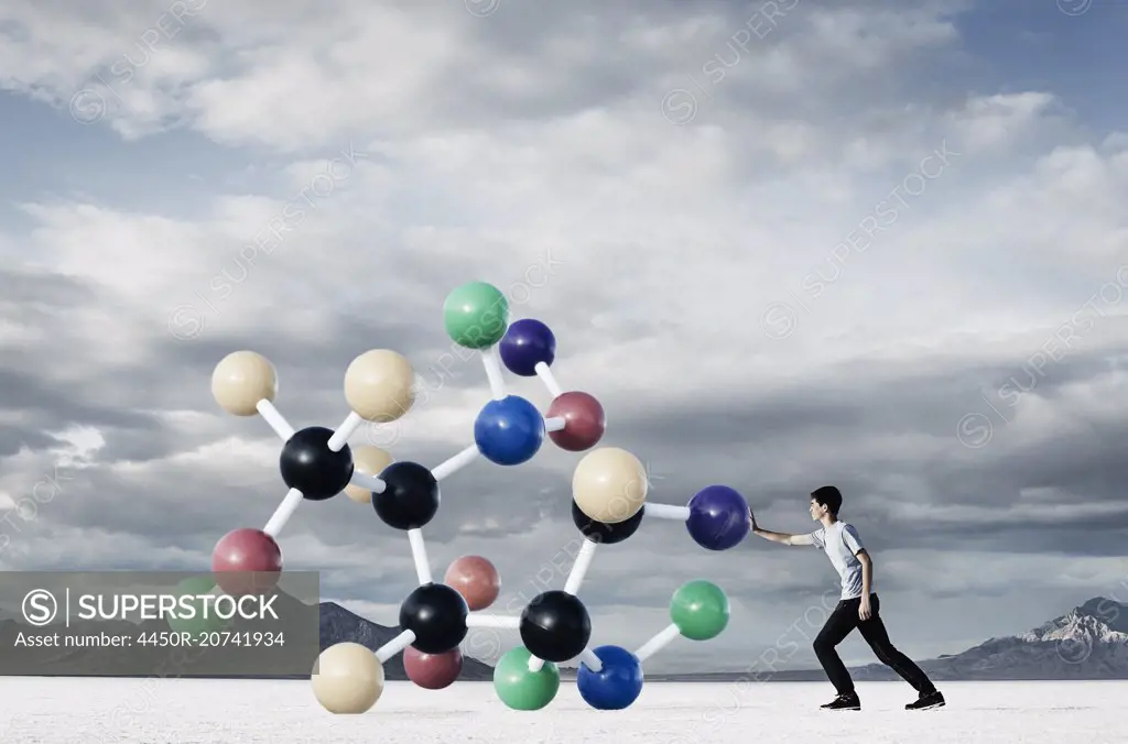 A teenage boy putting his hand out to push a large molecular structural model away from him.