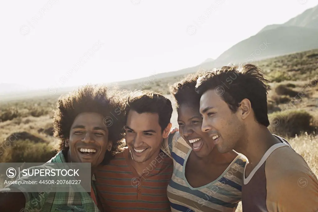 A group of friends, men and women, heads together posing for a selfy in the heat of the day.