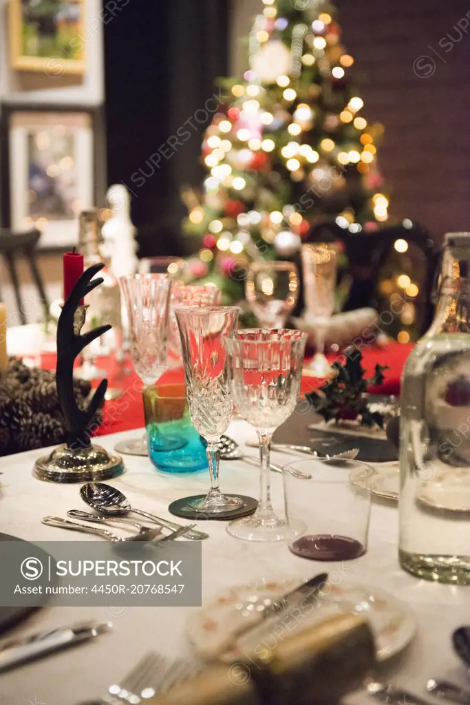 A table laid for a Christmas meal, with silver and crystal glasses and a Christmas tree in the background.