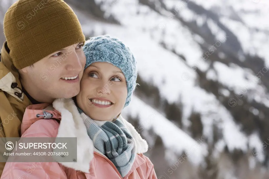 A couple hugging each other, a man and woman in the snowy mountains.