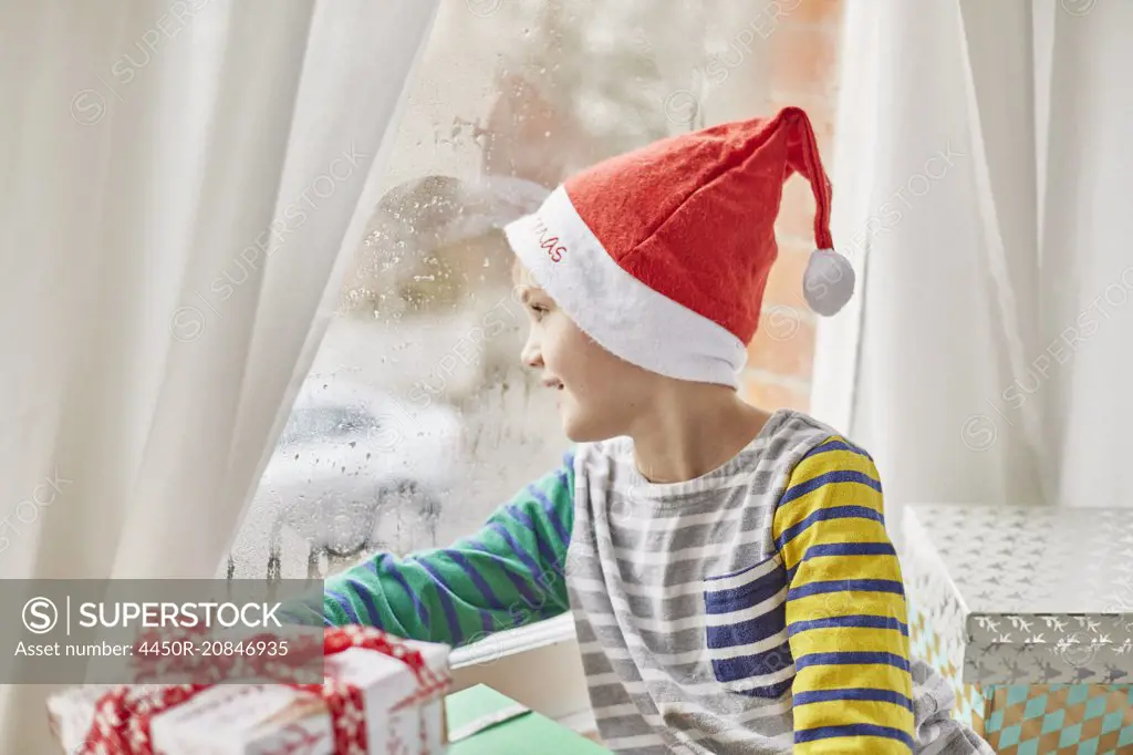 Christmas morning in a family home. A boy in a Santa hat looking out of a bedroom window.