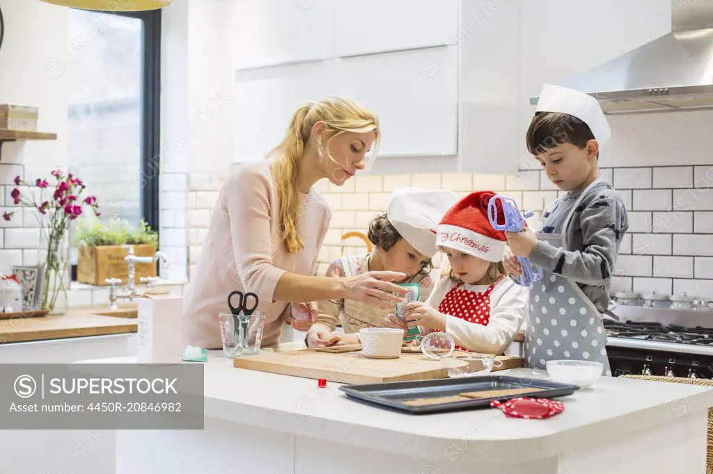 A woman and three children working together, making a gingerbread house, and icing the gingerbread.