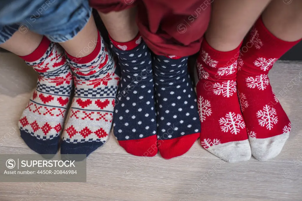 Three pairs of children's feet in bright patterned Christmas socks.