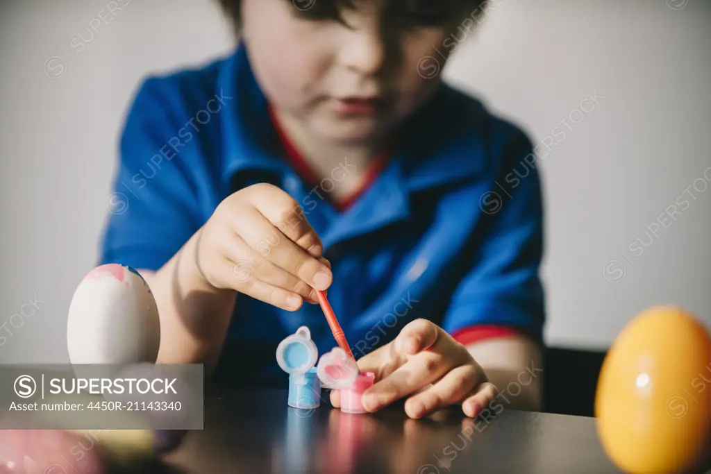 A boy sitting at a table decorating painting eggs.