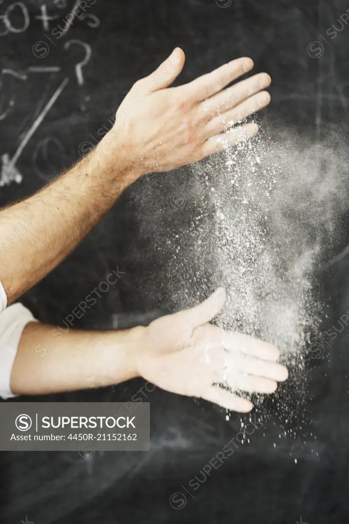 Close up of a baker standing in front of a blackboard, dusting his hands with flour.