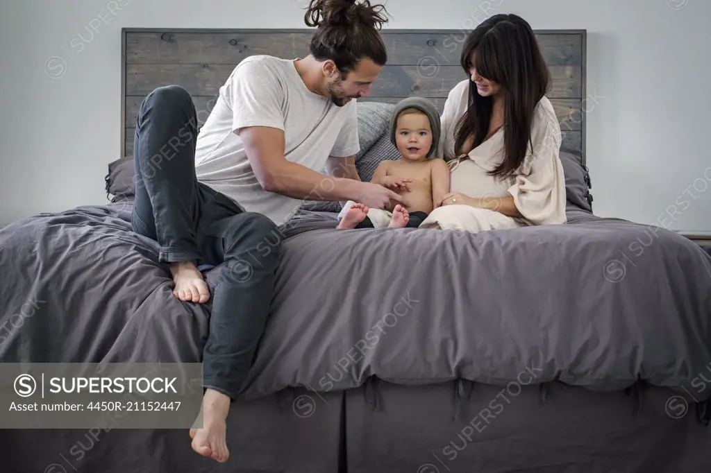 A young couple and their young son sitting together on their bed.