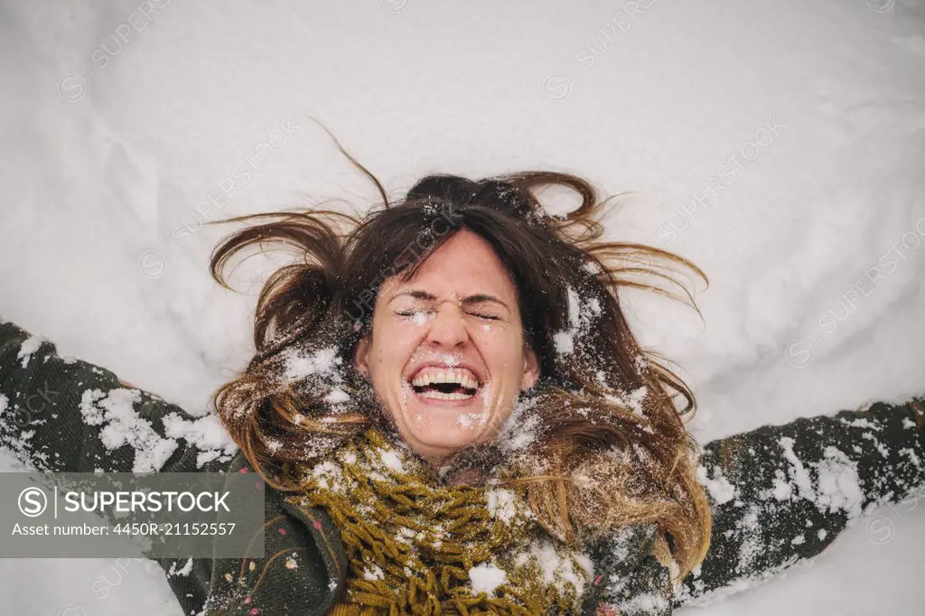 A woman lying on a snow bank with her arms stretched out.