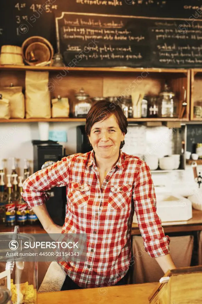 A woman in a coffee shop behind the counter, smiling, business owner.