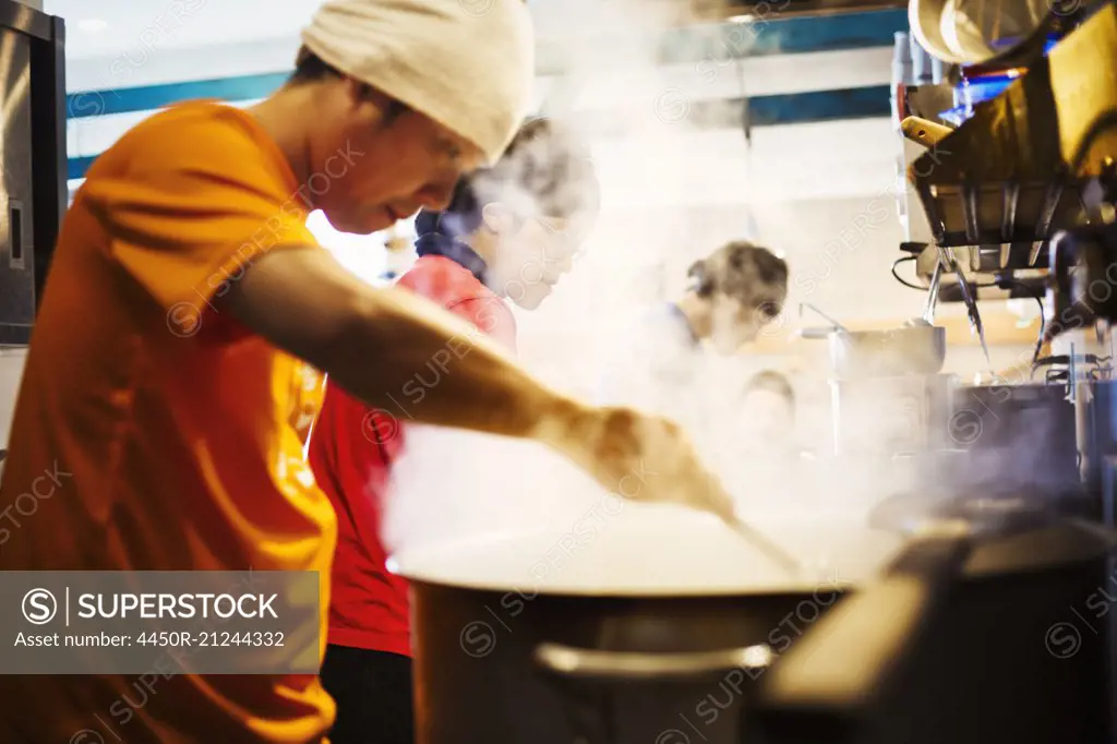 The ramen noodle shop. A chef stirring a huge pot of noodles cooking.