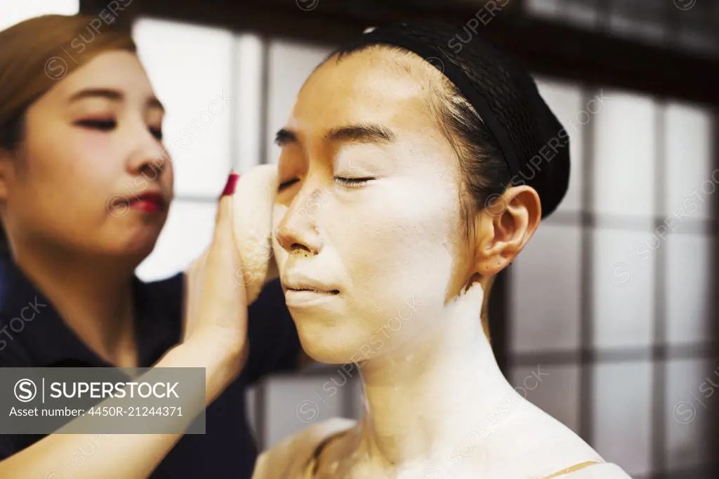 A modern geisha or maiko woman being prepared in traditional fashion, with white face makeup.