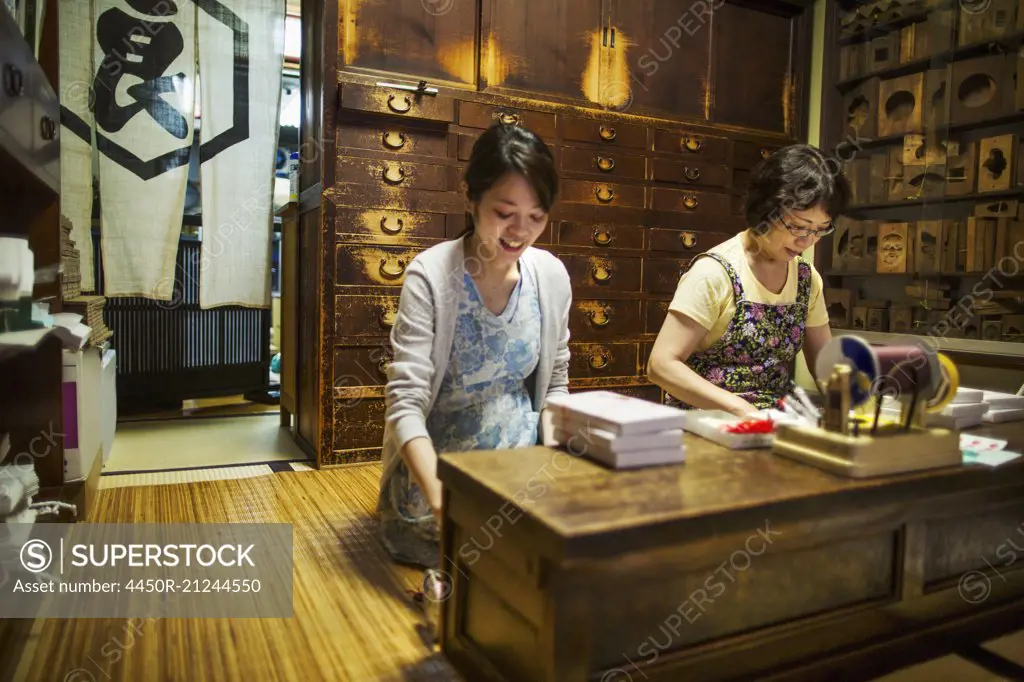 A traditional wagashi sweet shop. A woman working at a desk using a laptop and phone. A woman packing merchandise.