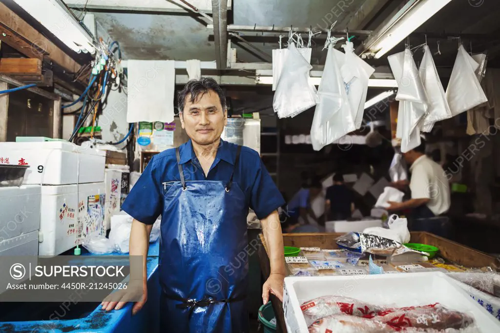 A traditional fresh fish market in Tokyo. A man in a blue apron standing behind the counter of his stall.