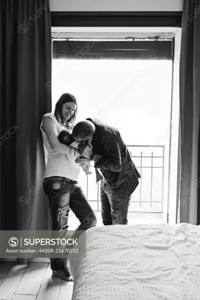 Parents standing in a bedroom cradling a small baby.