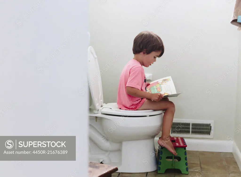 Boy, child sitting on toilet reading a book.