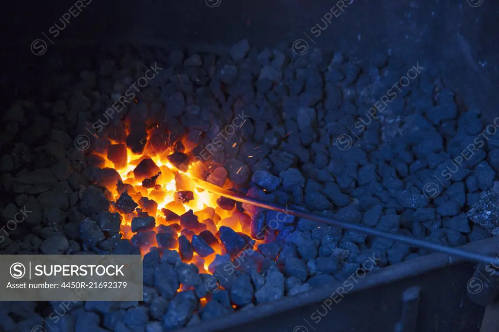 A glowing metal rod in the hot coals in a blacksmith's forge.