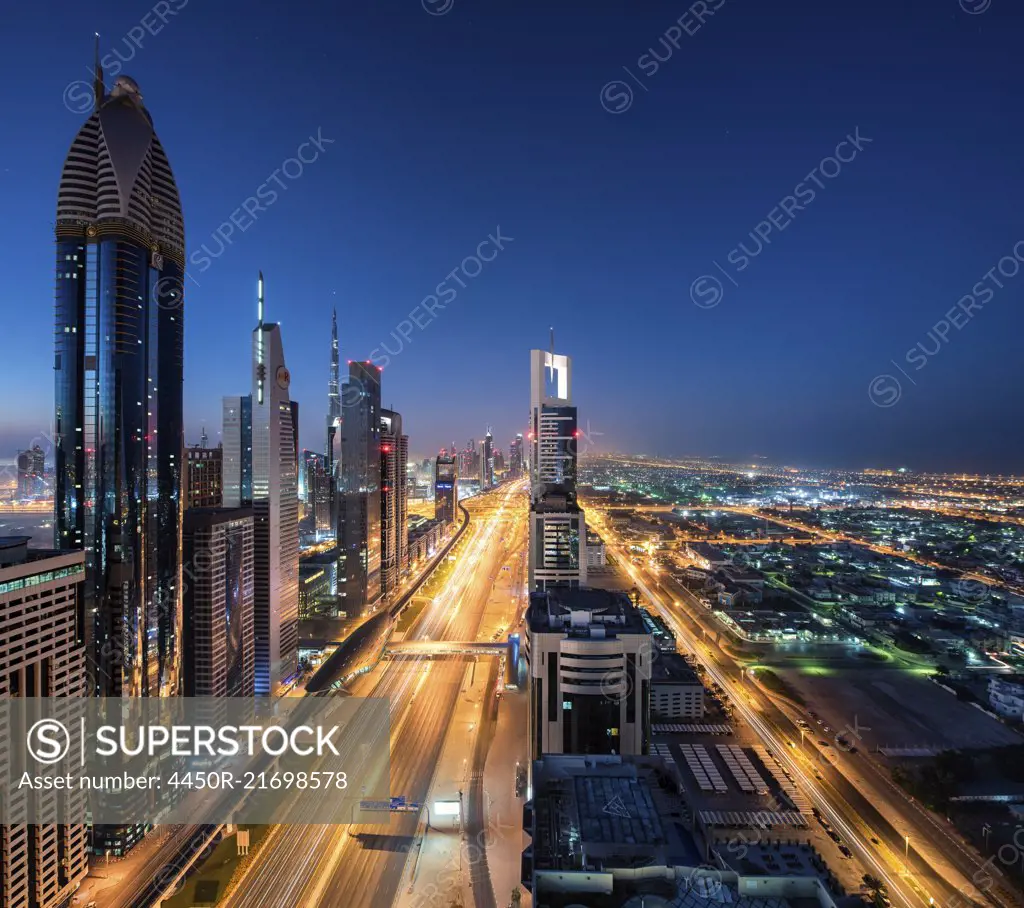 Cityscape of Dubai, United Arab Emirates at dusk, with skyscrapers lining illuminated street.