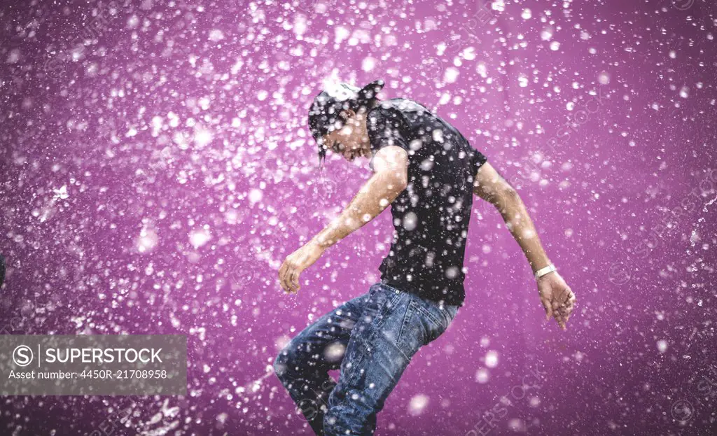 Young man standing in a shower of water drops.