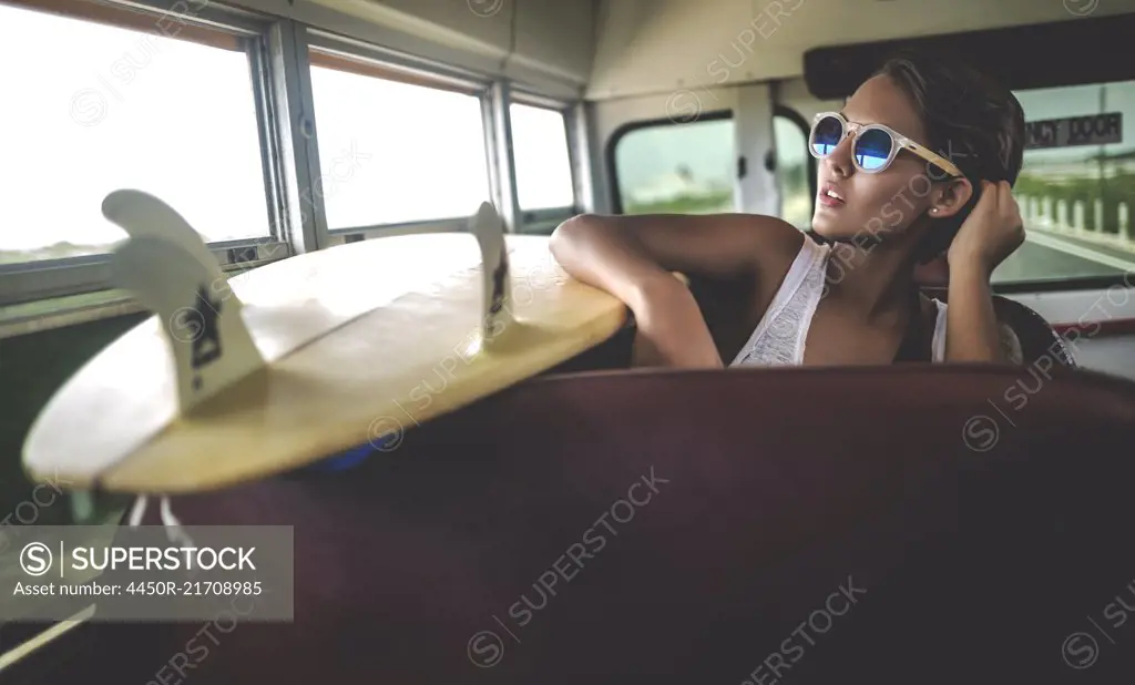 Young woman sitting on a bus with a surfboard.