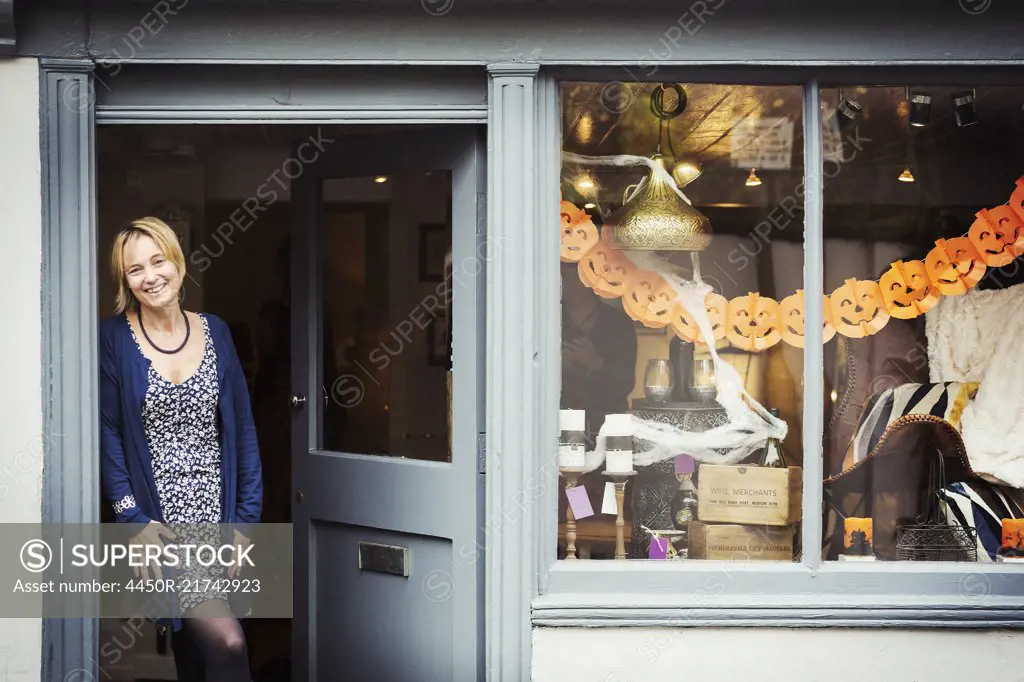 A woman standing in the doorway of her pop up interior design shop with a window display of objects.