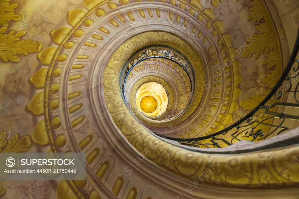 Low angle view of spiral staircase decorated with murals of golden Acanthus flowers and ornamental borders.