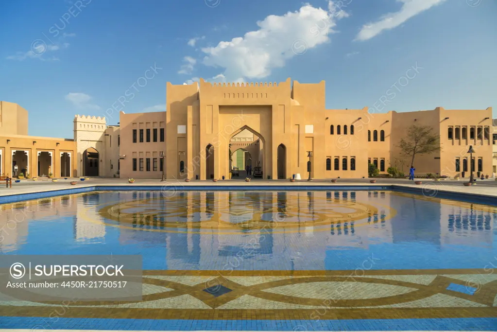 Facade of Middle Eastern building, pond with blue and golden mosaic tiles in foreground.